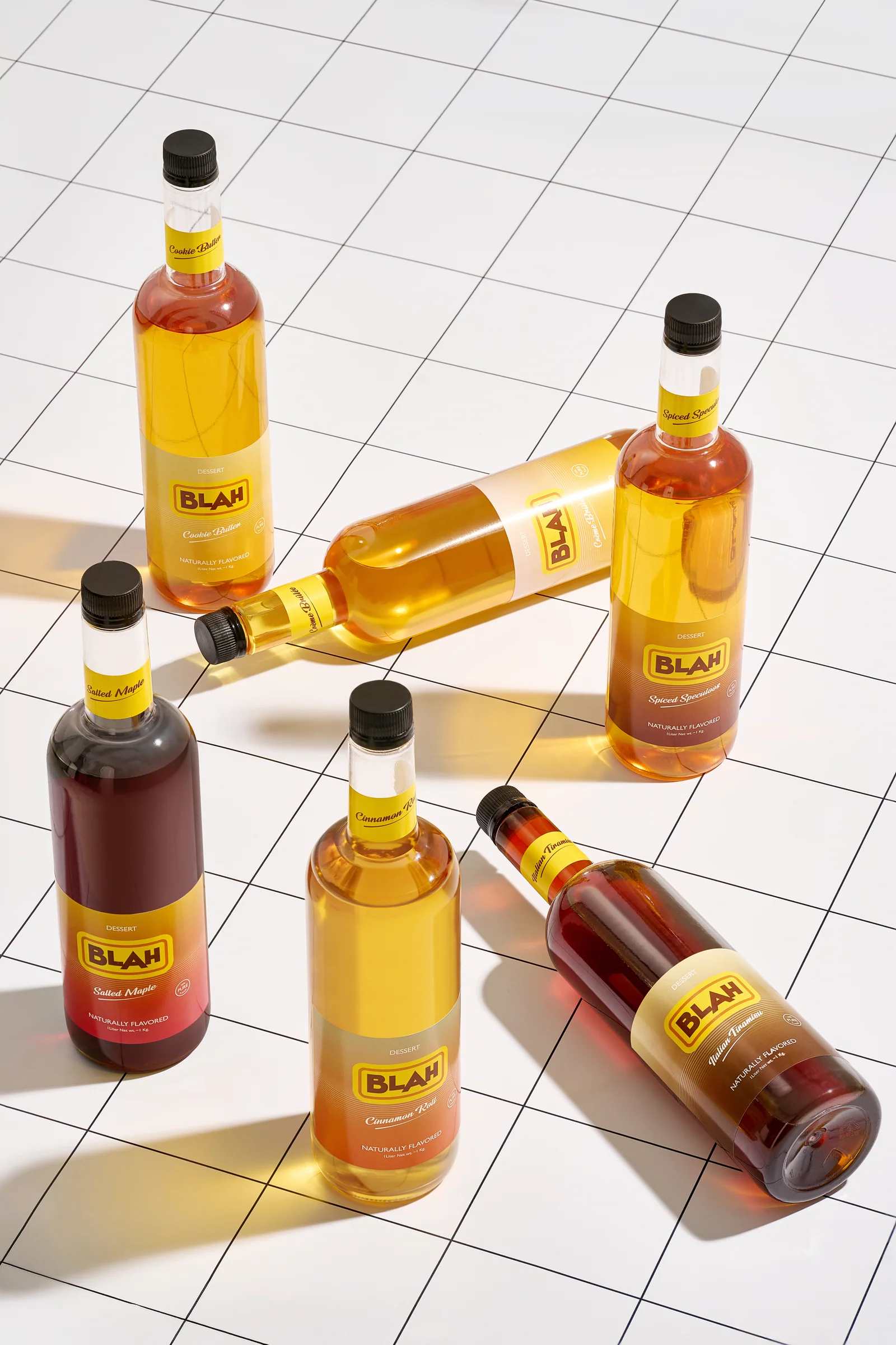 Six Blah dessert syrups scattered on a white grid-tile floor